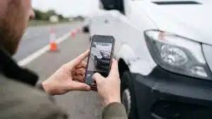 A fleet driver using a smartphone to photograph van damage at the roadside to capture complete incident data for a Fleet Response FNOL report.