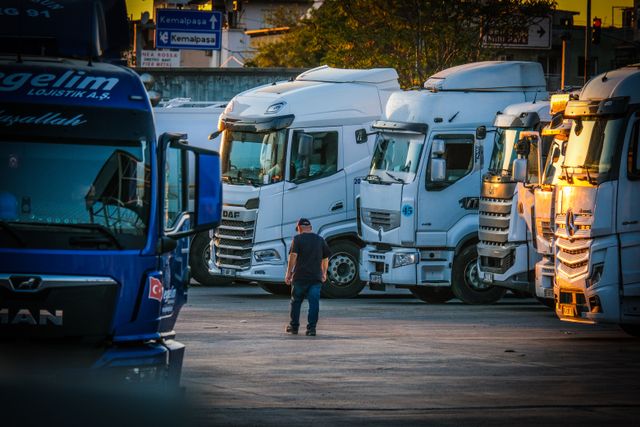 A fleet driver walking through a lot lined with large white and blue commercial transport trucks.