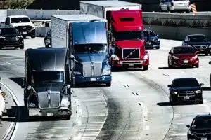 An high-angle photograph of commercial trucks and vehicles on a busy multi-lane highway, modified with a digital data overlay over the lead grey truck to represent predictive fleet safety analytics.