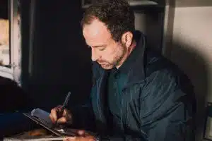 A commercial truck driver in a vehicle cabin carefully filling out paperwork on a clipboard, representing the initial driver intake and baseline MVR documentation process.