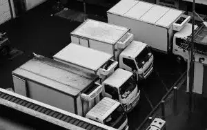 High-angle black and white shot of several white commercial delivery trucks parked in a lot, representing fleet management and DOT compliance.