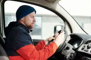 man using smartphone in van A commercial fleet driver sitting in the cab of his service van, looking at a smartphone to complete an immediate corrective training module or report a road incident.