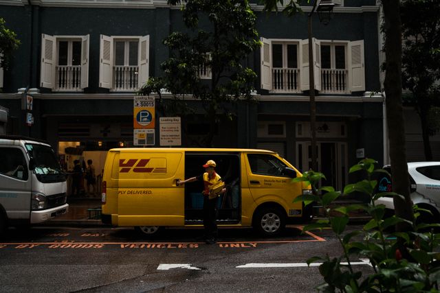 A delivery driver holding packages while opening the side door of a yellow commercial delivery van parked in a loading bay.